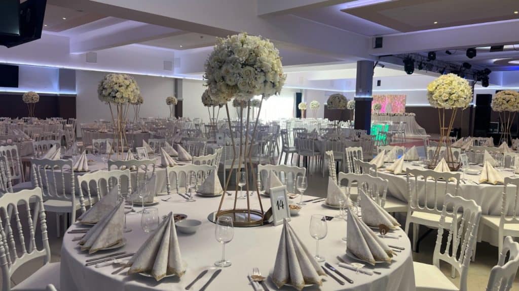 Hochzeitslocation: Ein Bankettsaal mit weißen Tischen und Stühlen, der sich perfekt für Hochzeiten eignet.